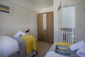 Habitación de hotel con dos camas, un armario de madera, un espejo y una puerta que da a otra habitación.
