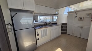 Una cucina compatta con mobili bianchi, un frigorifero in acciaio inox, un forno a microonde e una finestra con vista sull'acqua.