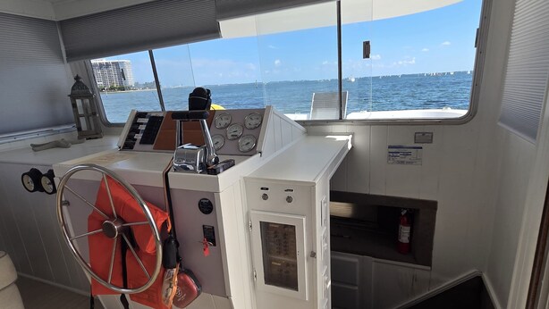 Interni di una barca con un pannello di controllo, un timone e vista sul mare.