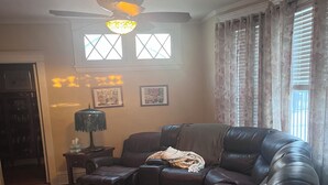 A living room with a sectional sofa, a ceiling fan, a lamp, and a window with curtains. - NFL draft come stay at Serene 5-bedroom house with in charming Pittsburgh (Pittsburgh)