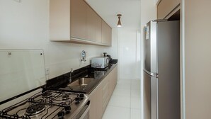 A modern kitchen with a gas stove, stainless steel appliances, and beige cabinetry. - Apto c Garagem e Ar Condicionado na Praia do Sul (Ilhéus)