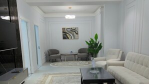 A modern living room with a sofa, two armchairs, a coffee table, a TV, and a painting on the wall. - Cozy 2-bedroom condo in lovely Toshkent with AC (Тоshkent)
