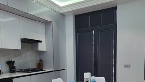 A modern kitchen with white cabinets, a black stove, and a dining area with a round table and white chairs. - Cozy 2-bedroom condo in lovely Toshkent with AC (Тоshkent)