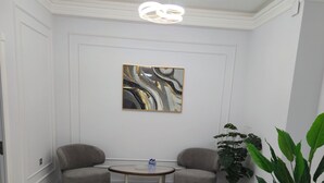 A living room with a round coffee table, two armchairs, a modern chandelier, a large abstract painting, and a potted plant. - Cozy 2-bedroom condo in lovely Toshkent with AC (Тоshkent)