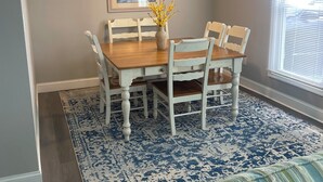 A dining area with a wooden table, white chairs, a vase with yellow flowers, a ceiling fan, and a patterned rug. - 3-bedroom 2 BA Coastal Ranch house New Castle with long driveway (Wilmington Manor)