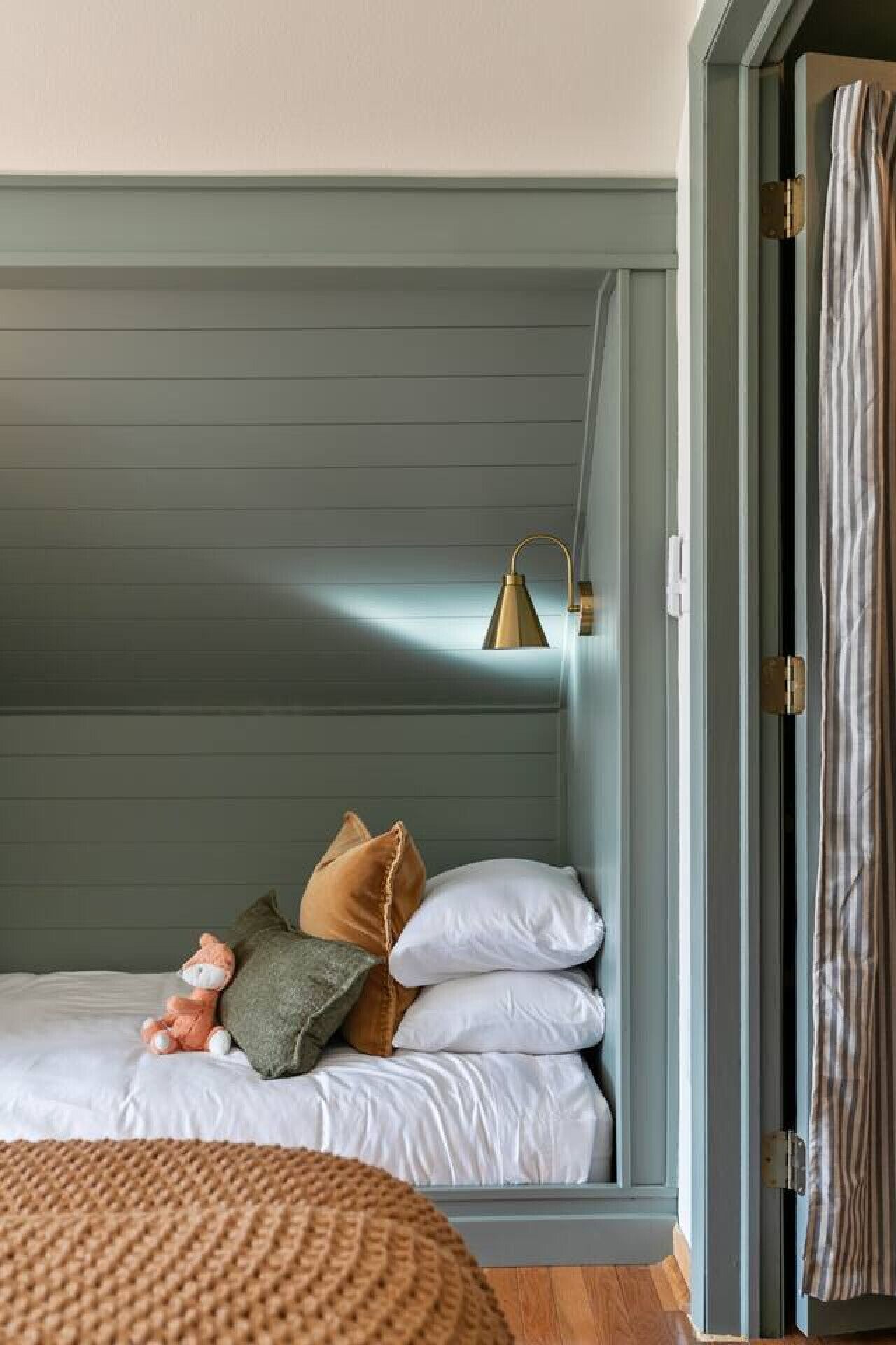 A cozy bedroom with a bed, pillows, a small stuffed animal, a lamp, and a window with curtains.