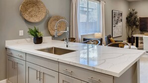 Una cocina moderna con una isla grande, pileta de acero inoxidable y alacenas de color gris claro.
