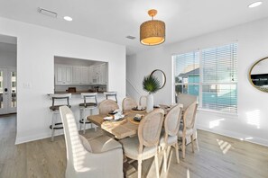 A dining area with a wooden table, six chairs, and a hanging light fixture. - Bella Vacanza • Minutes to Beach • Community Pool (Gulf Shores)
