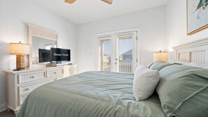 Un dormitorio con cama, cómoda, televisor, ventilador de techo y una ventana con persianas.