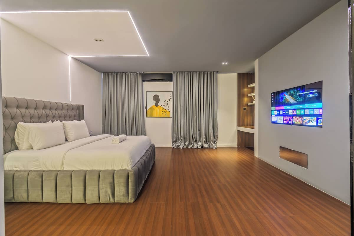 A modern bedroom with a large bed, a flat-screen TV mounted on the wall, and a wooden floor.