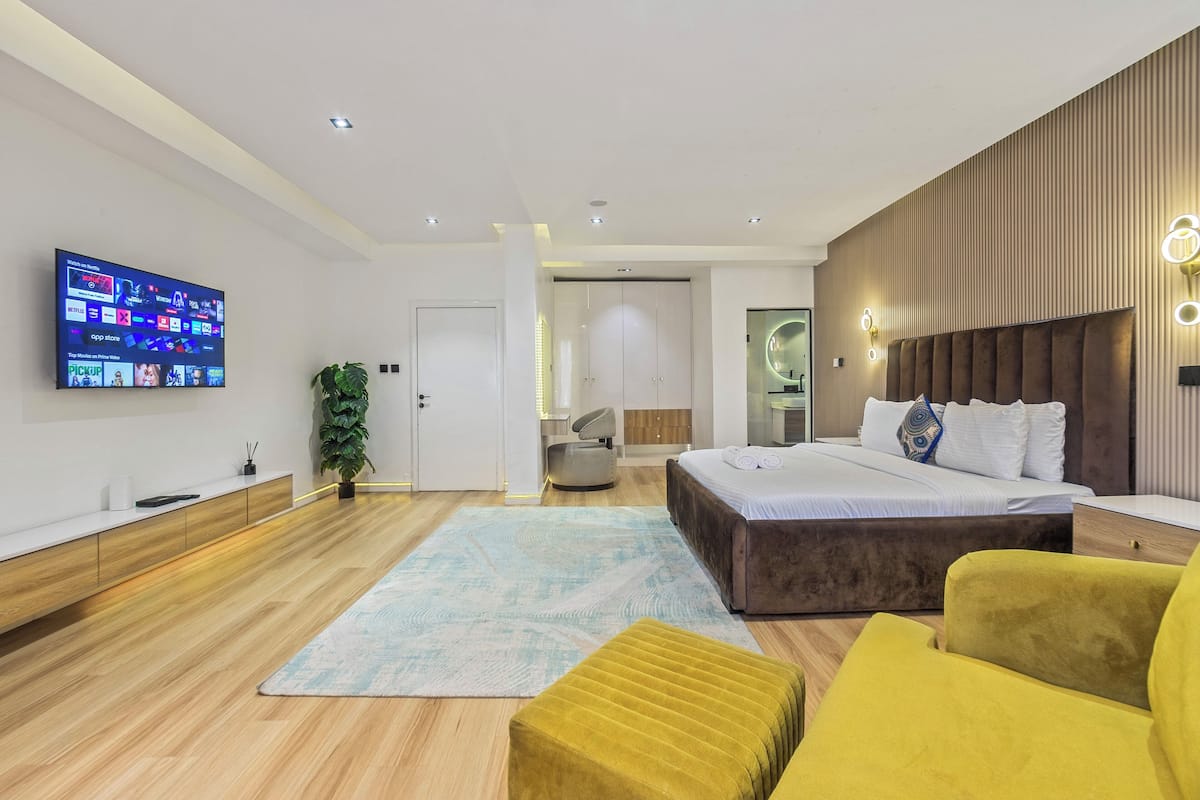 A modern bedroom with a large bed, a TV mounted on the wall, and a wooden headboard.