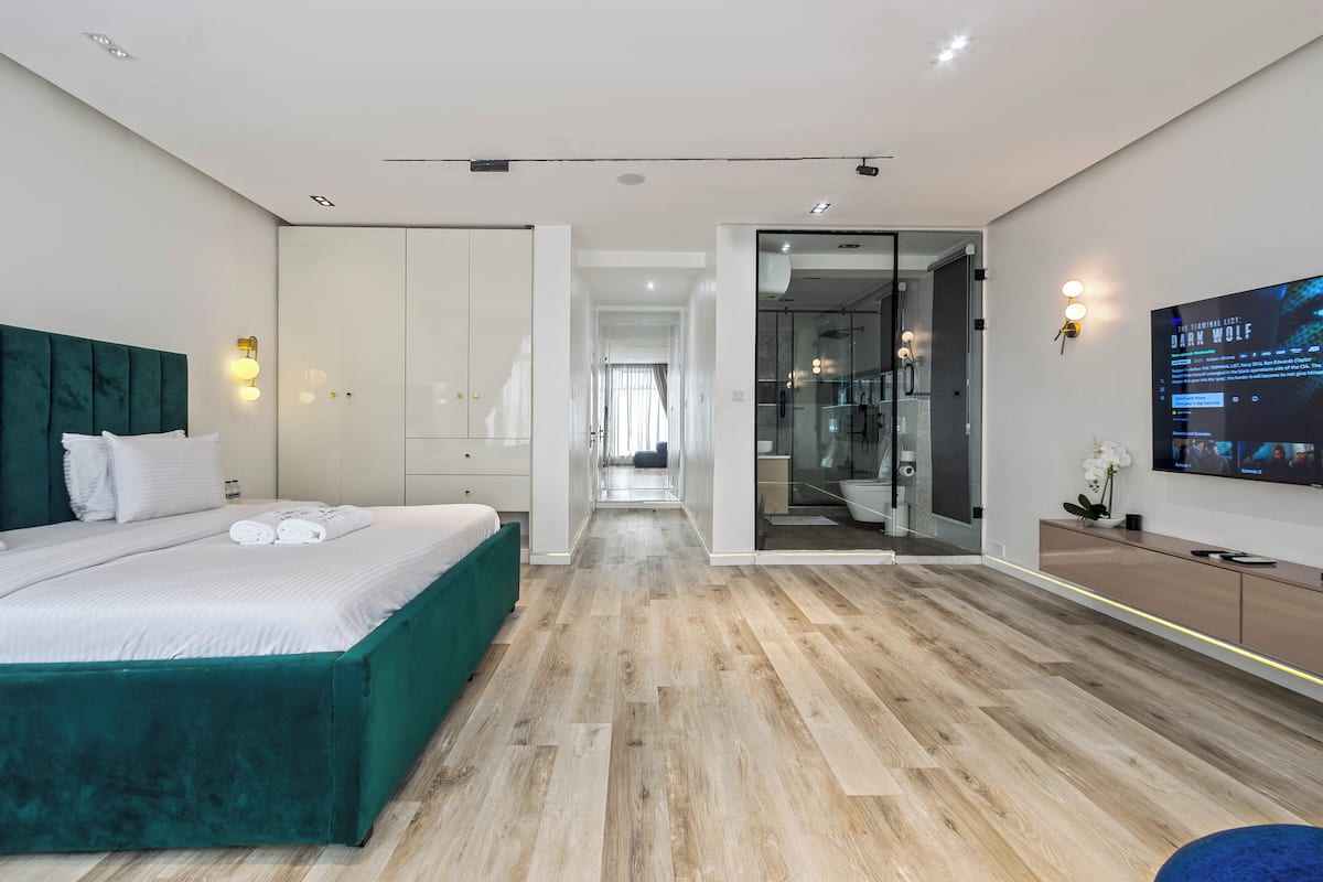 A modern hotel room with a large bed, a TV, and a bathroom visible through a glass door.