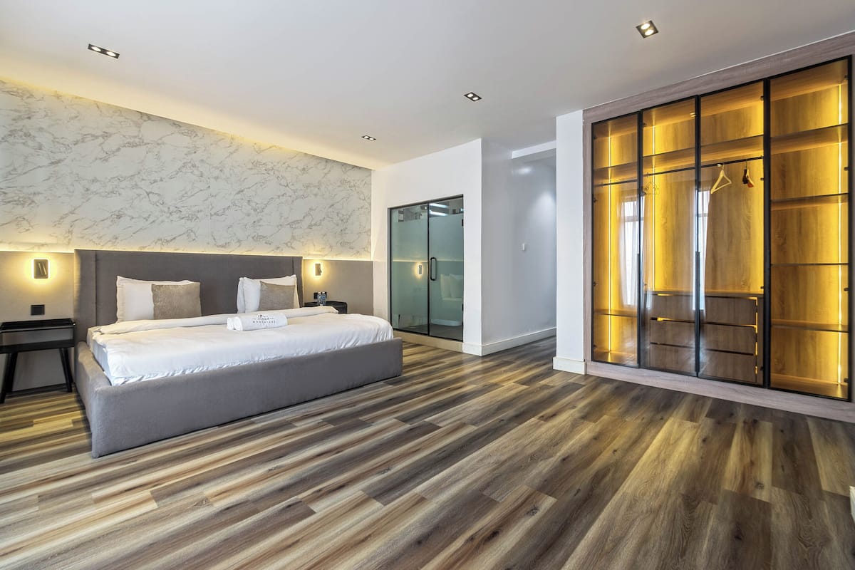 A modern bedroom with a large bed, a walk-in closet, and a glass door shower.