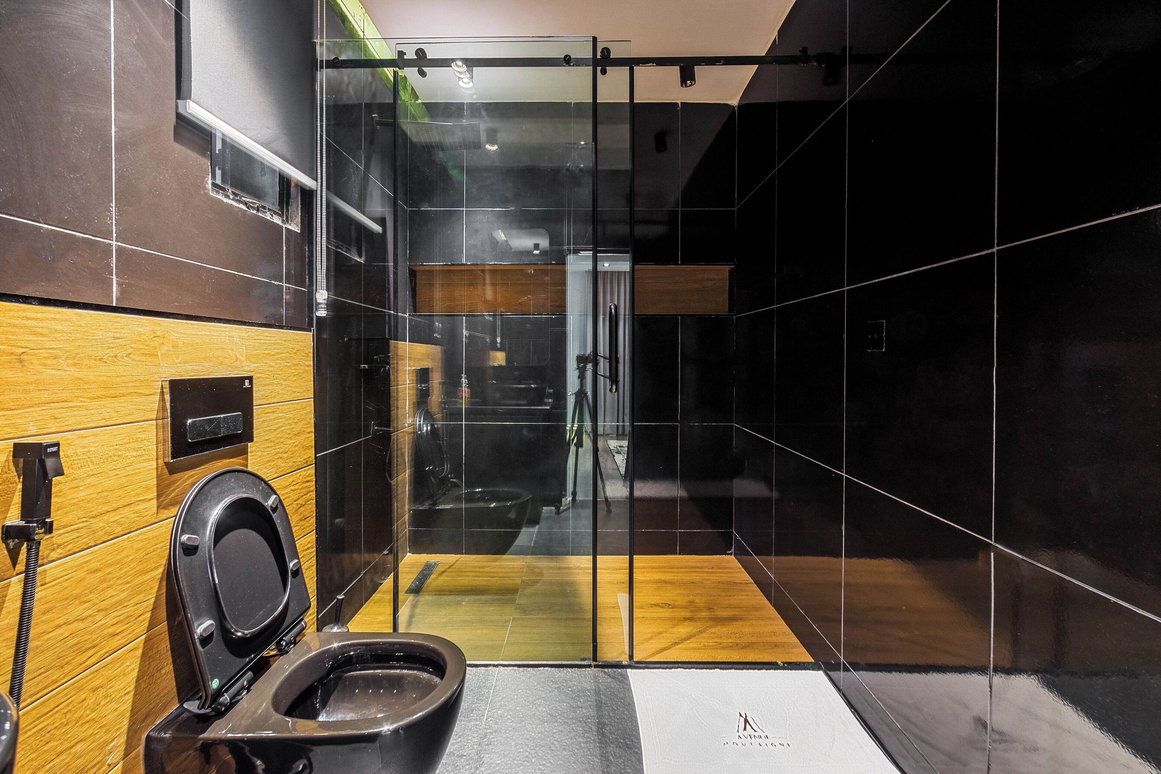 A modern bathroom with a glass partition, a wooden vanity, and a black toilet.