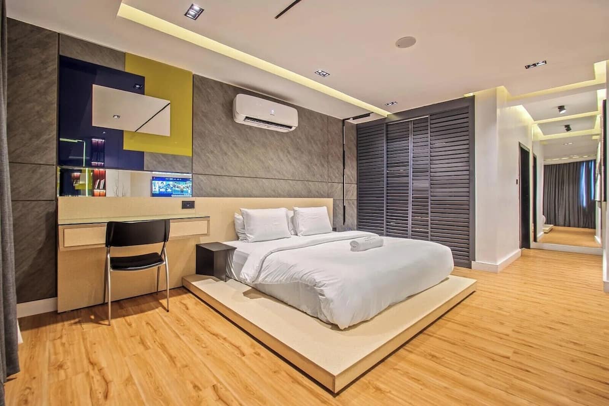 A modern hotel room with a large bed, a desk with a chair, a flat-screen TV, and an air conditioning unit.
