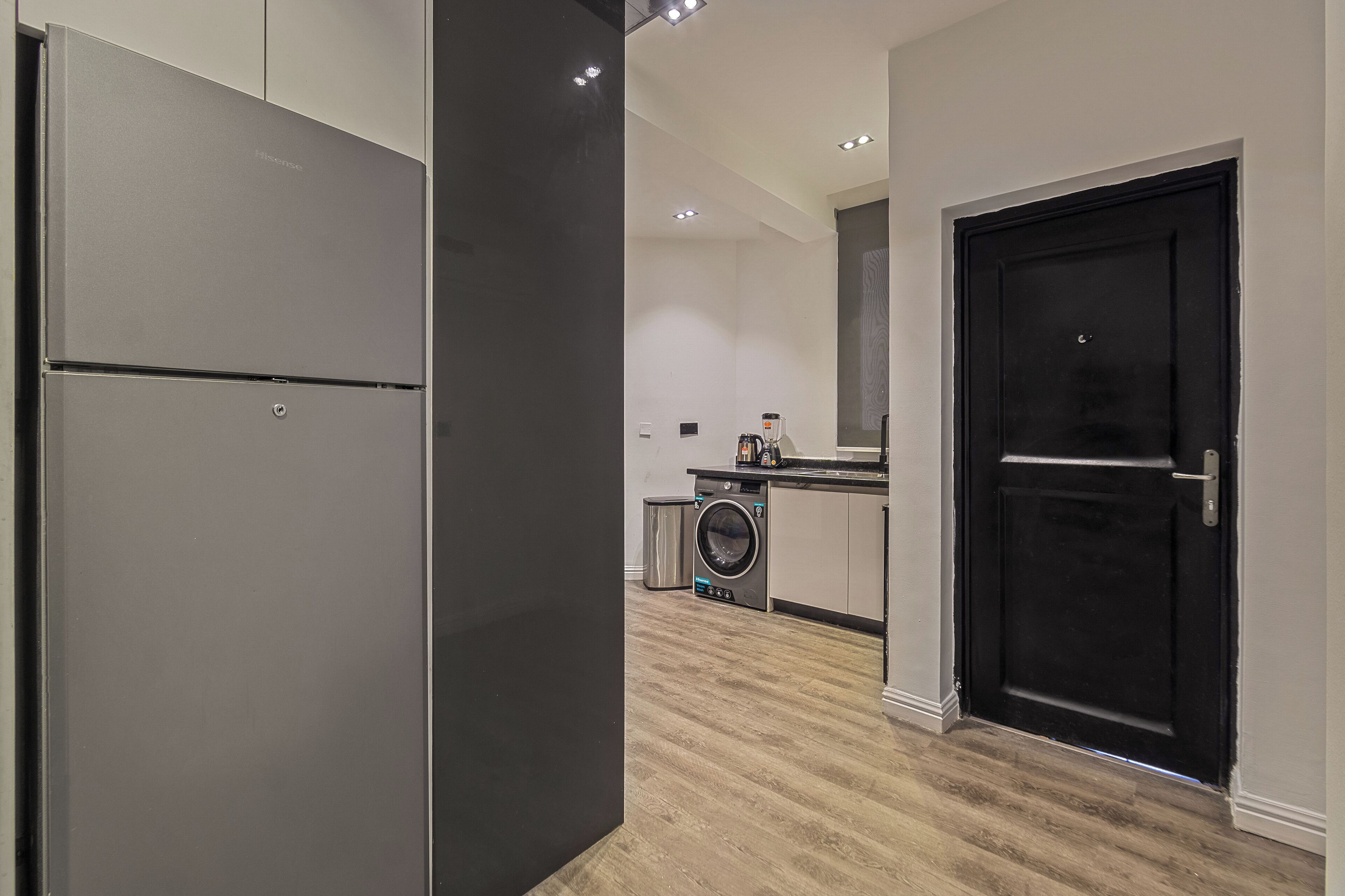 A modern kitchen with a stainless steel refrigerator, a washing machine, and a black door.