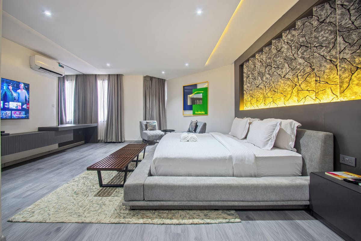 A modern bedroom with a large bed, a TV, a seating area, and a decorative wall.