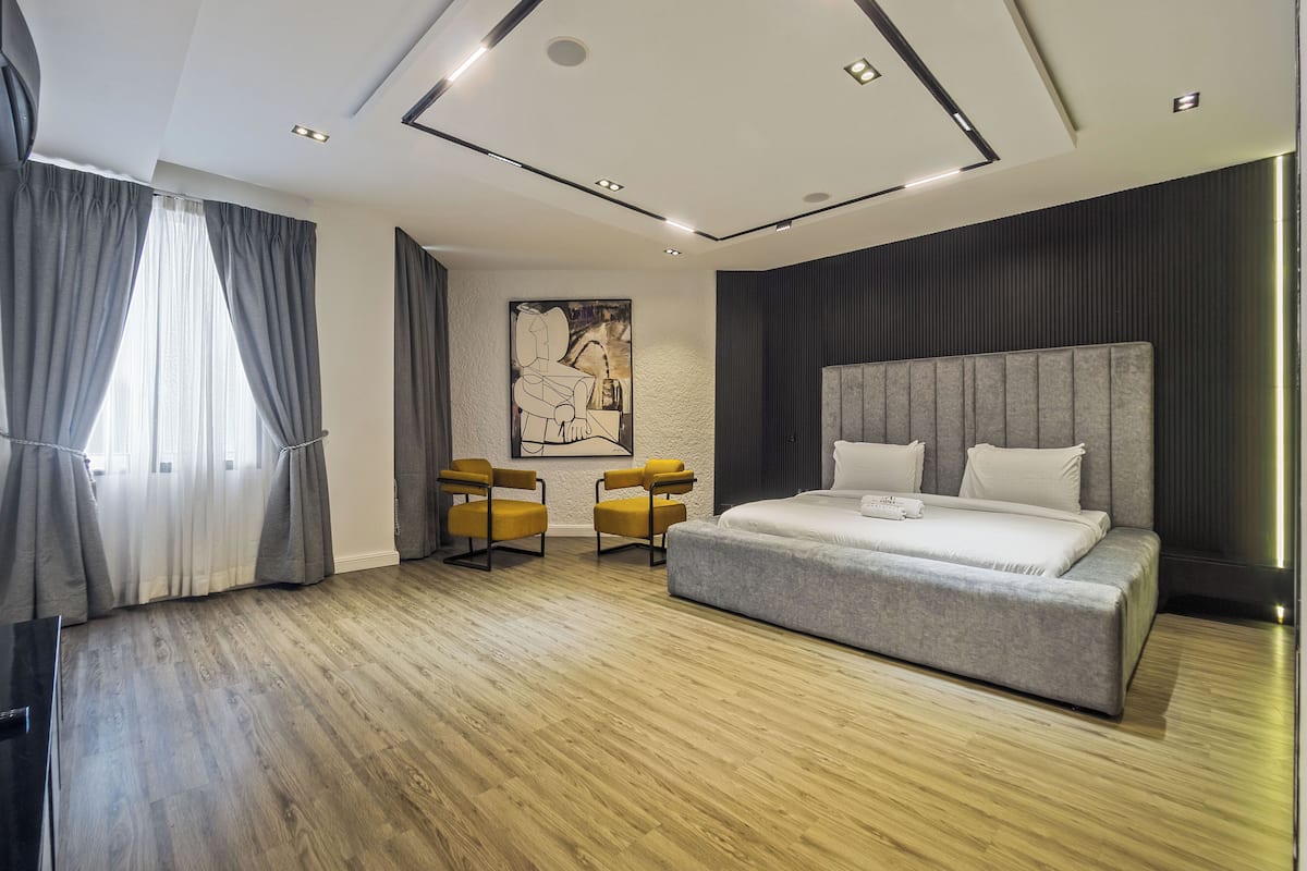 A modern bedroom with a large bed, two chairs, wooden flooring, and a ceiling with recessed lighting.
