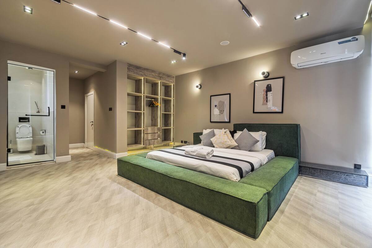 A modern bedroom with a large bed, built-in shelving, and an air conditioning unit.
