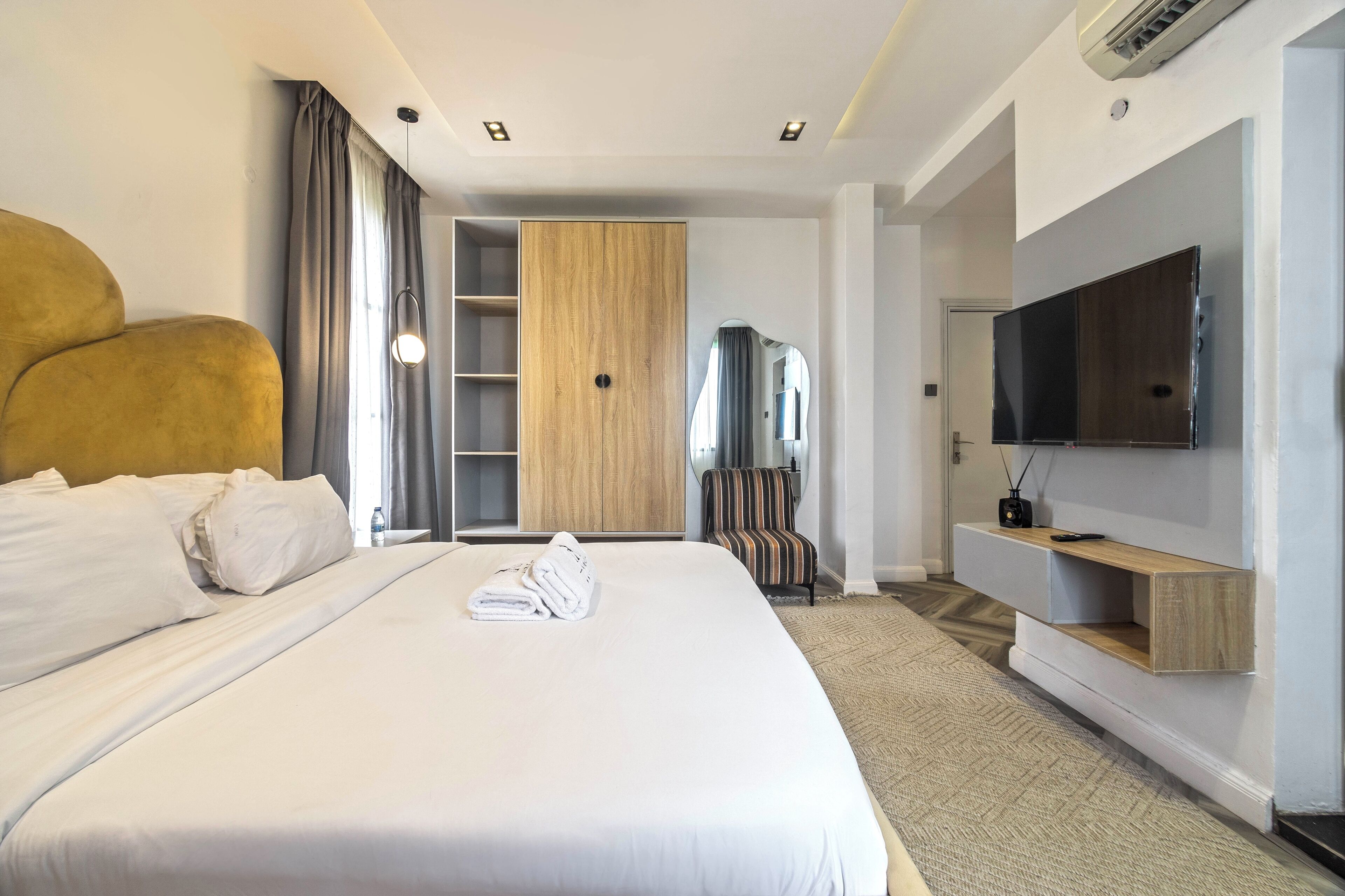 A hotel room with a large bed, a wardrobe, a TV, and a small seating area.
