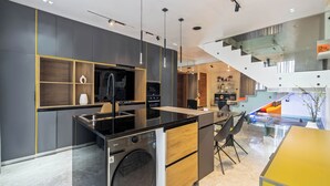 Une cuisine moderne équipée d’un lave-linge et d’un sèche-linge intégrés, un coin repas avec une table jaune, et un escalier menant à un niveau supérieur.