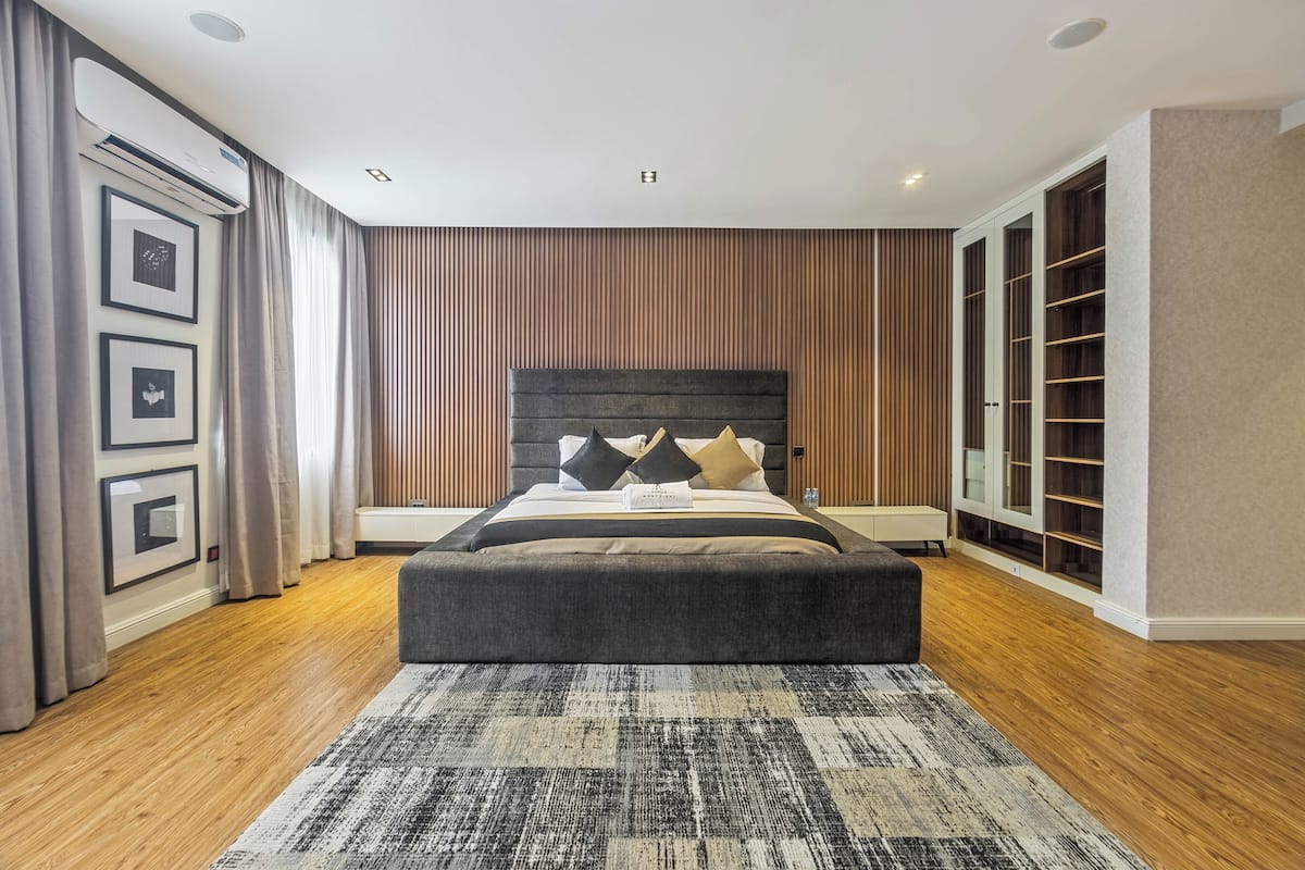 A modern bedroom with a large bed, a wooden headboard, a built-in wardrobe, and a patterned rug.