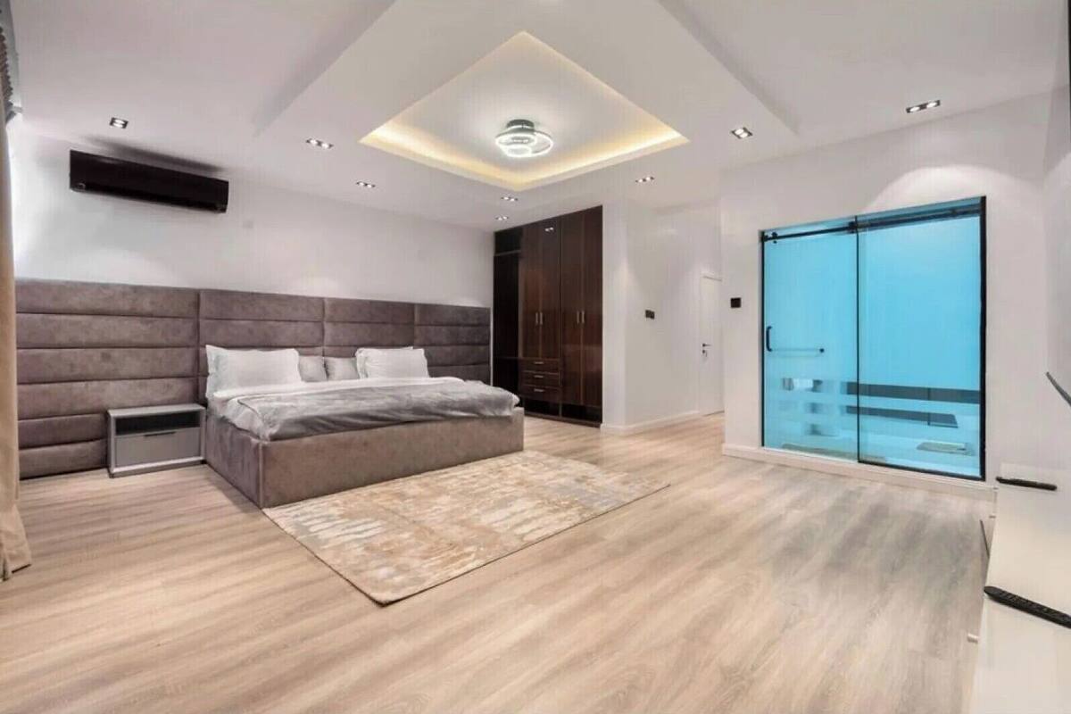 A modern bedroom with a large bed, a built-in bench, a ceiling light, and a sliding glass door to a balcony.