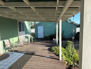 Une véranda couverte avec un plancher en bois, des sièges d’extérieur et un petit espace jardin.
