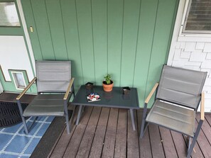 Un petit espace extérieur aménagé avec deux chaises et une table, un pot de fleurs et une porte dotée d’une fenêtre.