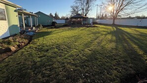 Ein gepflegter Garten mit Rasen, einem Pavillon und einem Haus mit Veranda.