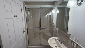 A bathroom with a glass-enclosed shower, a sink, and a mirror.