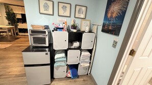 A compact kitchenette with a microwave, toaster, and refrigerator. There are framed pictures on the wall and a poster of fireworks.