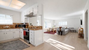 Eine moderne Küche mit weißen Schränken, einem eingebauten Backofen und einer Mikrowelle. Es gibt einen Essbereich mit Tisch und Stühlen sowie ein Wohnzimmer mit einer Couch und einem Fernseher.