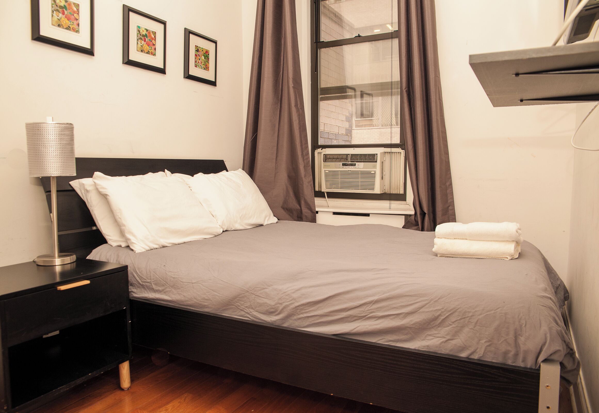 A neatly made bed with white linens, a bedside table with a lamp, and a window with curtains.