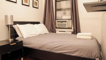 A neatly made bed with white linens, a bedside table with a lamp, and a window with curtains.