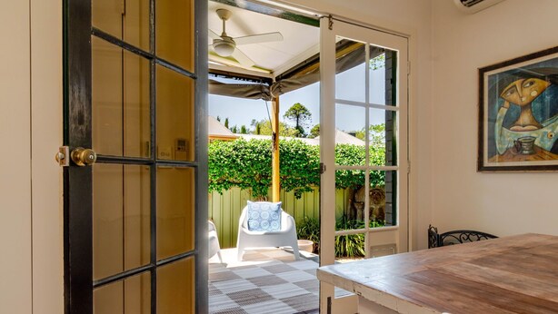 Eine offene Tür, die auf eine Terrasse mit Deckenventilator, einem weißen Stuhl und einem Tisch führt.