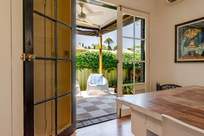 Une porte ouverte donnant sur un patio équipé d’un ventilateur de plafond, d’une chaise blanche et d’une table.