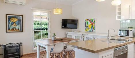 A modern kitchen with a central island, white cabinetry, a built-in microwave, and a flat-screen TV.