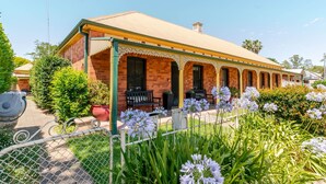 Ein Backsteinhaus mit gelbem Dach, einer Veranda mit Bänken und einem Garten mit weißen Blumen.