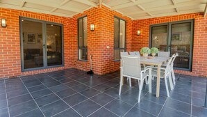 Een overdekt terras met een bakstenen muur, grote schuifdeuren en een tafel met stoelen.