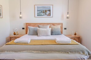 Ein ordentlich bezogenes Bett mit einem Holzkopfteil, zwei Nachttischen mit Lampen und einem gerahmten Bild an der Wand.