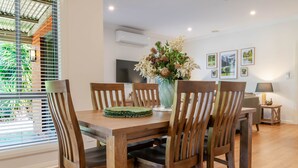 Een eetruimte met een houten tafel en stoelen, een vaas met bloemen en lijstjes met foto's aan de muur.