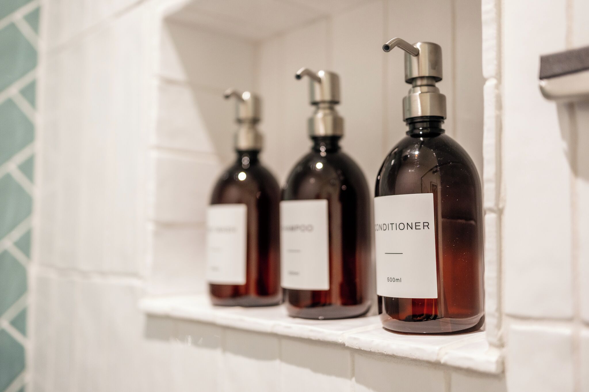 Three bottles of conditioner on a white shelf in a bathroom.