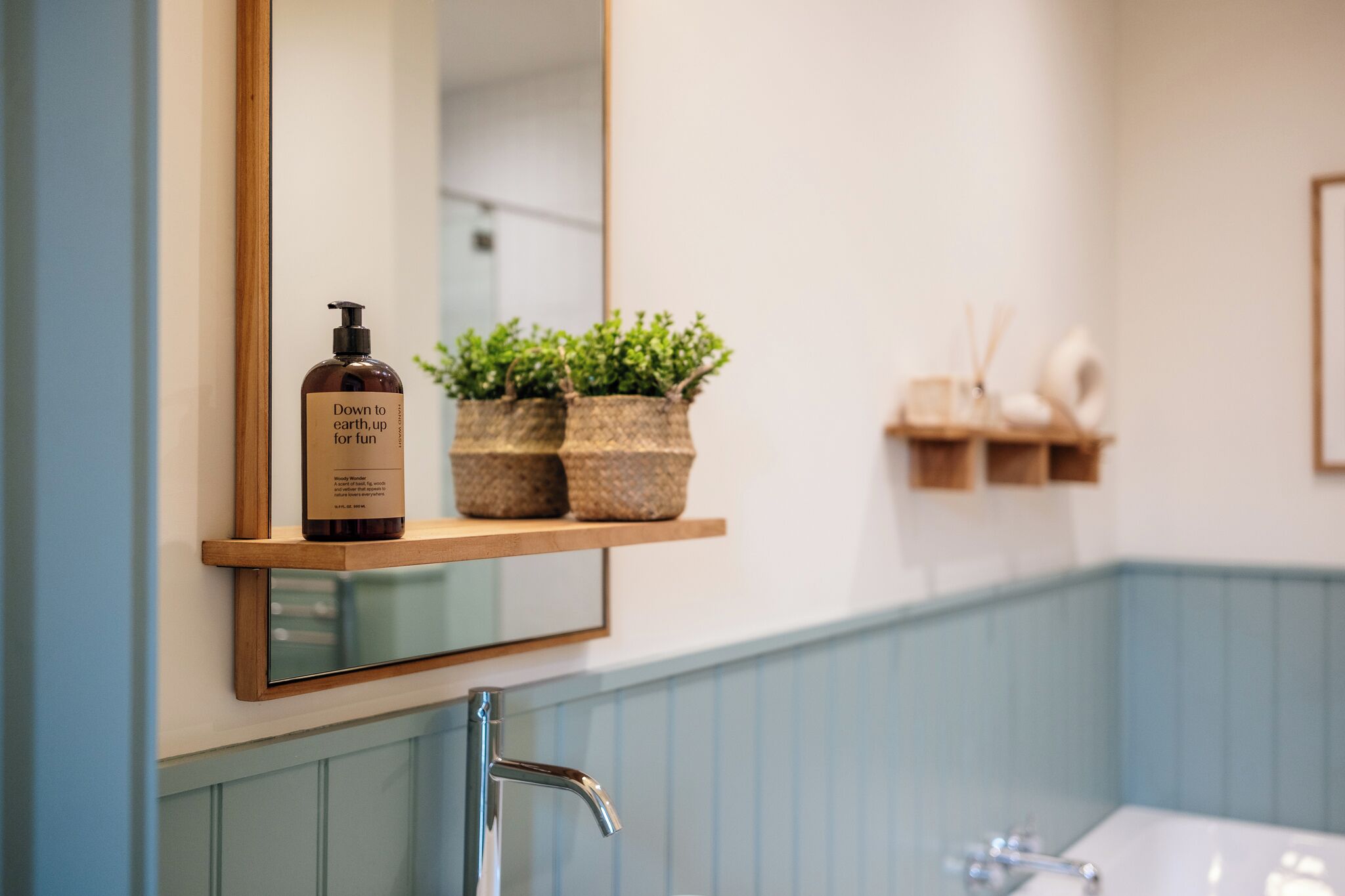 A bathroom with a wooden shelf holding a bottle and two potted plants.