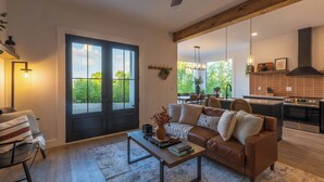 Un salon moderne avec un canapé en cuir marron, une table basse sur laquelle sont posés des livres et une grande fenêtre donnant sur un paysage verdoyant.