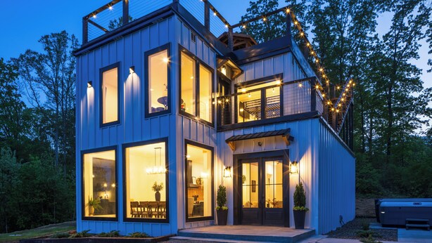 Une maison moderne à deux étages, dotée de grandes fenêtres, d’un balcon et de guirlandes lumineuses.