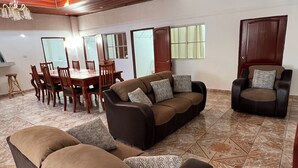 Un amplio salón con un conjunto de sofá marrón, una mesa de comedor con sillas, un ventilador de techo y un ventanal grande.