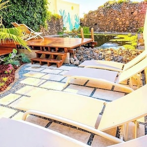 Un espace aménagé au bord de la piscine, avec des chaises longues, une terrasse en bois et un mur en pierre.