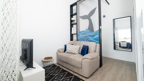 Ein Wohnzimmer mit einer Couch, einem Fernseher, einer Wand mit einem typischen Wal-Schwanz-Muster und einem Spiegel.