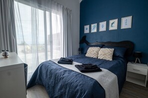 A bedroom with a large bed, a bedside table, a nightstand, and a window with curtains. - Guest Suite ("Baleias") near PDL (Sao Roque)